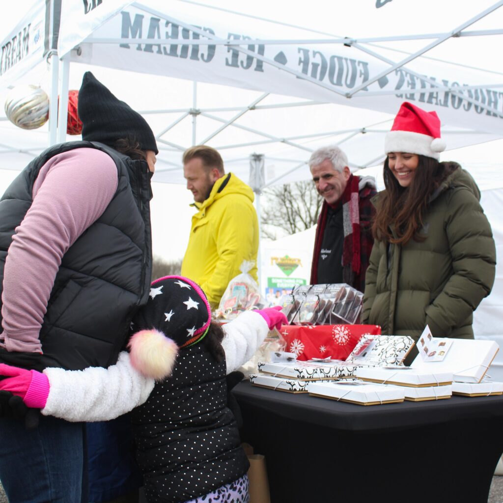 a mother and her child buy chocolates from a winter festival vendor