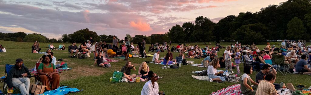 Music in the Meadow concert attendees sitting in the Ellipse Meadow at sunset, formatted as a newsletter banner