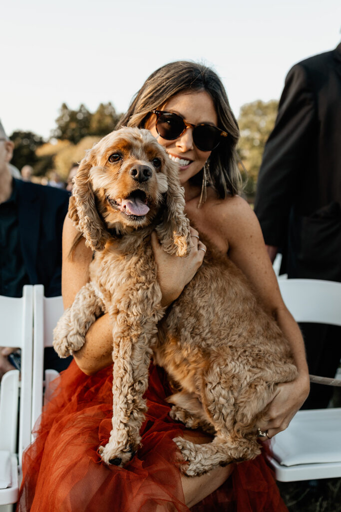 a wedding guest holding a dog at the outdoor ceremony