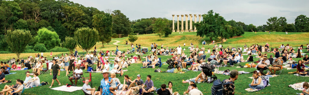 concert attendees sitting in the ellipse meadow on picnic blankets, with the capitol columns in the background, formatted as a newsletter banner