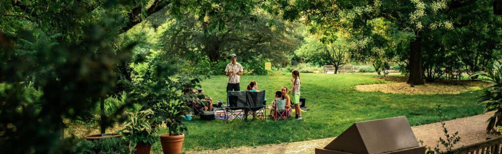 summer evening guests having a picnic in the herb garden, formatted as a newsletter banner