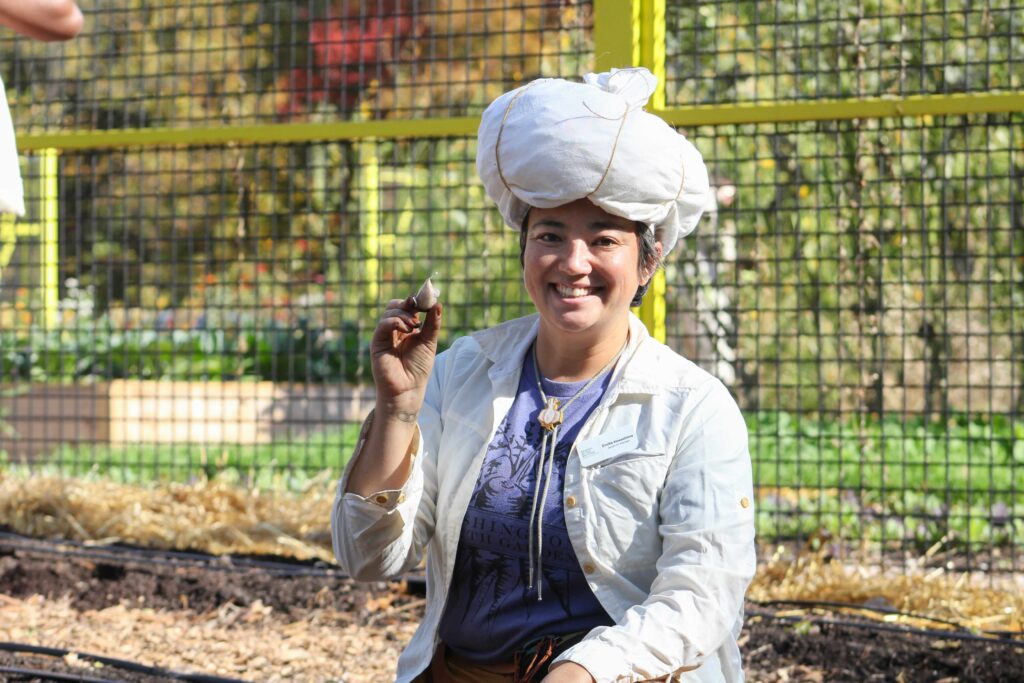 emilia holding up garlic wearing a garlic outfit at the garlic planting party