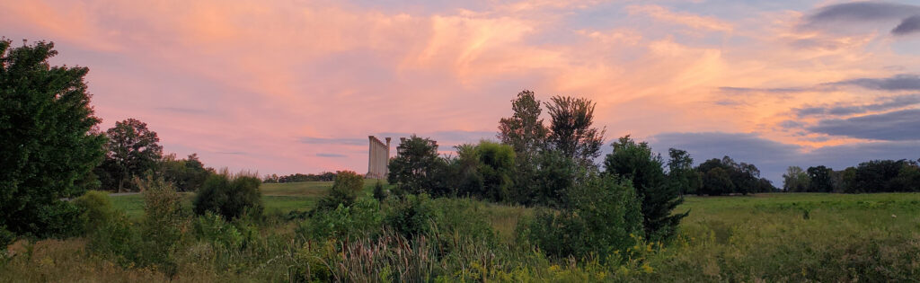 The sun sets over a meadow at the National Arboretum, with the National Capitol Columns in the distance