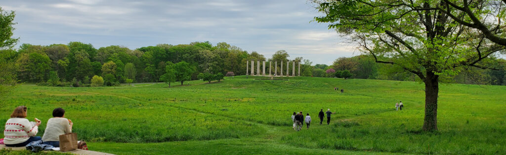 Two people sit in a grassy meadow looking at the National Capitol Columns at the National Arboretum
