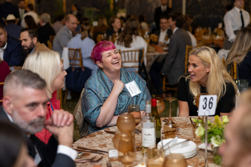 A dinner under the stars guest laughing at a dinner table while talking to people at the table